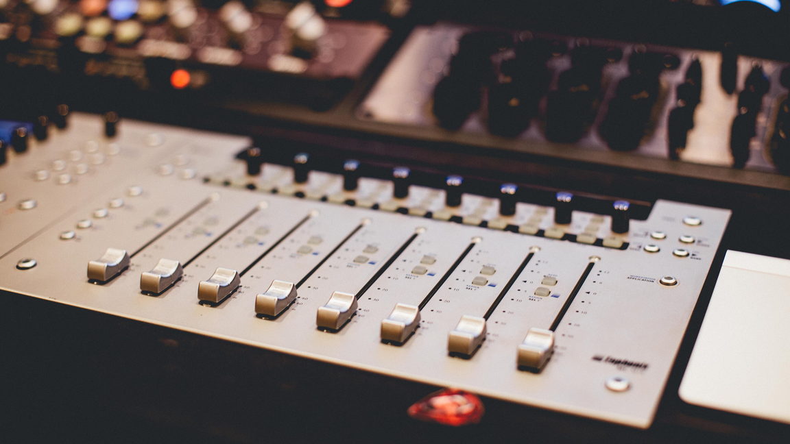 A mixing console in a darkened control room, its channel strips picked out by coloured indicator lights.