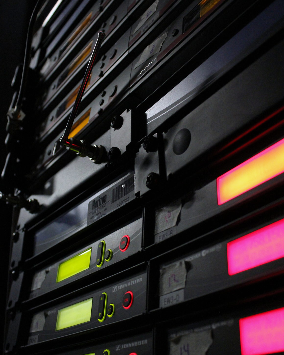 A tall equipment rack in a dark room, its receiver displays lit green and amber.
