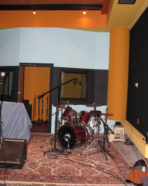 Drum kit miked and ready in a live room, control-room window behind