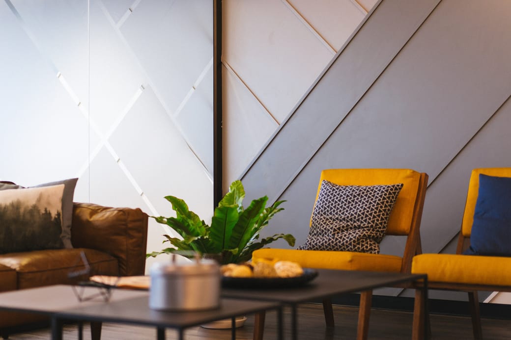 A tan leather sofa and two yellow armchairs around a low table beside a potted plant.