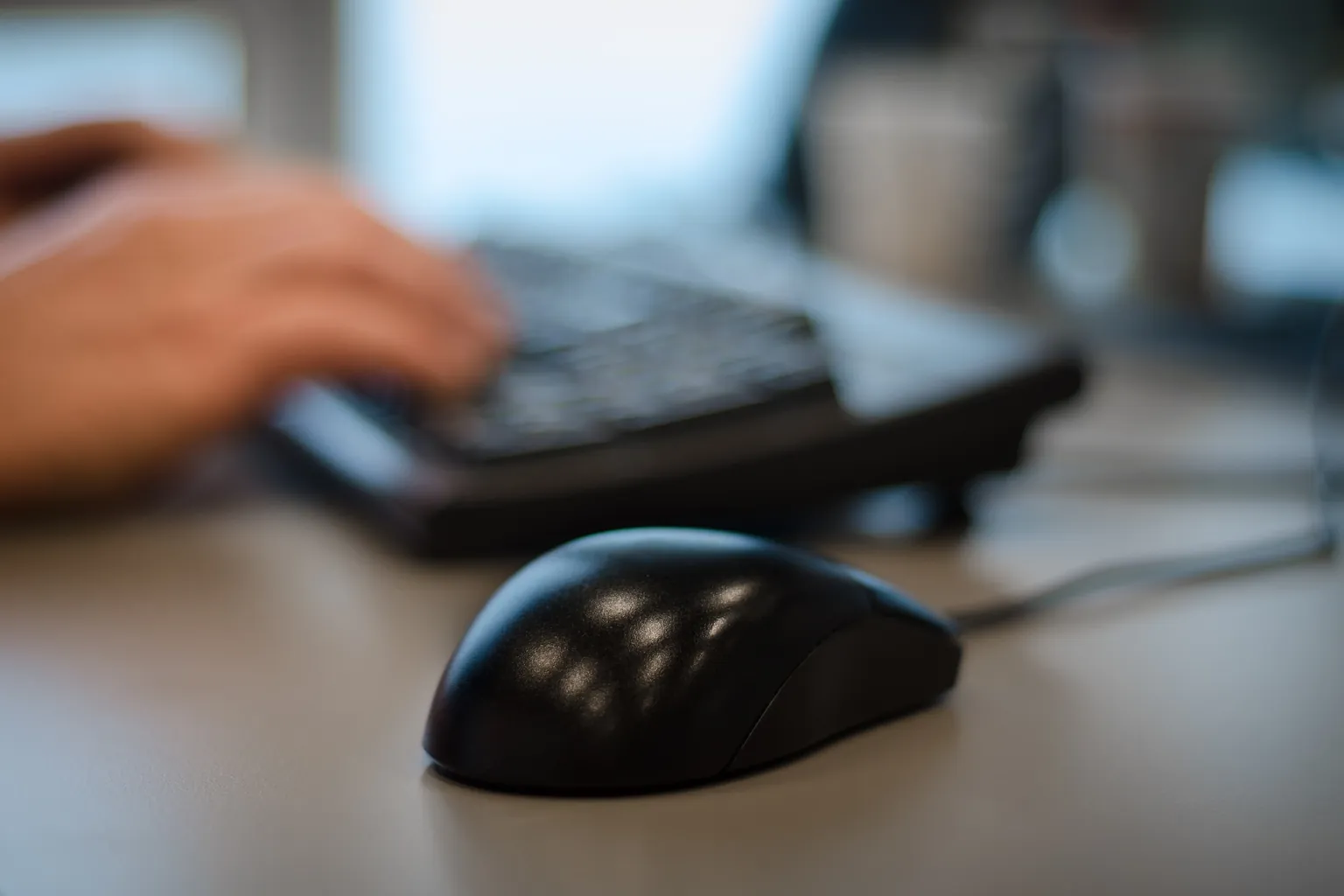 Hands at a keyboard and mouse on a cleared day desk