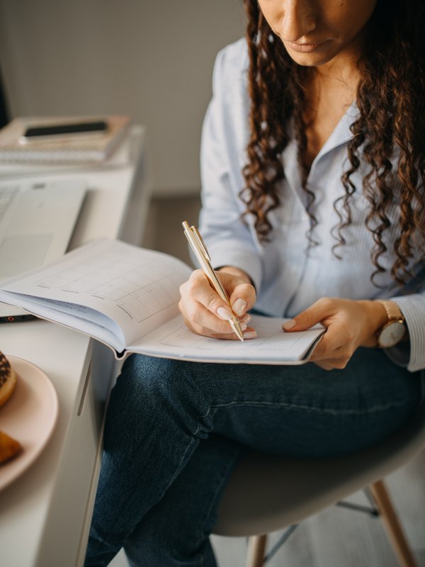 A member taking notes beside her laptop at a desk