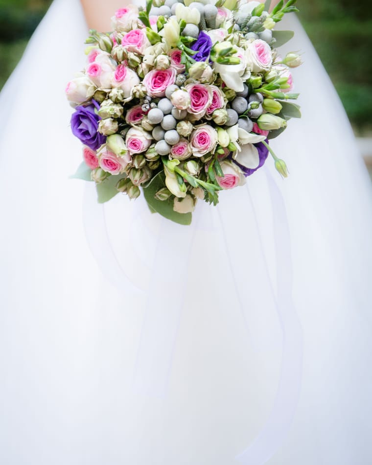 A compact bouquet of cream roses held in front of a white bridal dress.