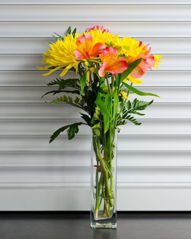Yellow and orange alstroemeria arranged in a clear glass vase on a studio bench.