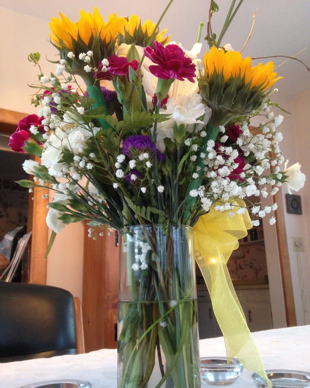 A mixed vase of sunflowers and carnations finished with a yellow ribbon.