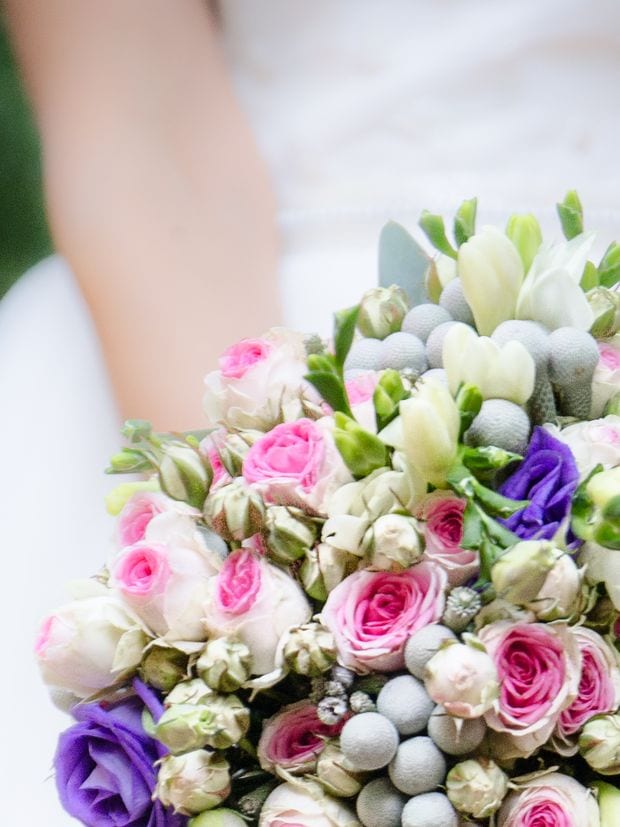 A bridal bouquet of pink roses, white freesia and silver brunia, held so the wearer stays out of frame.