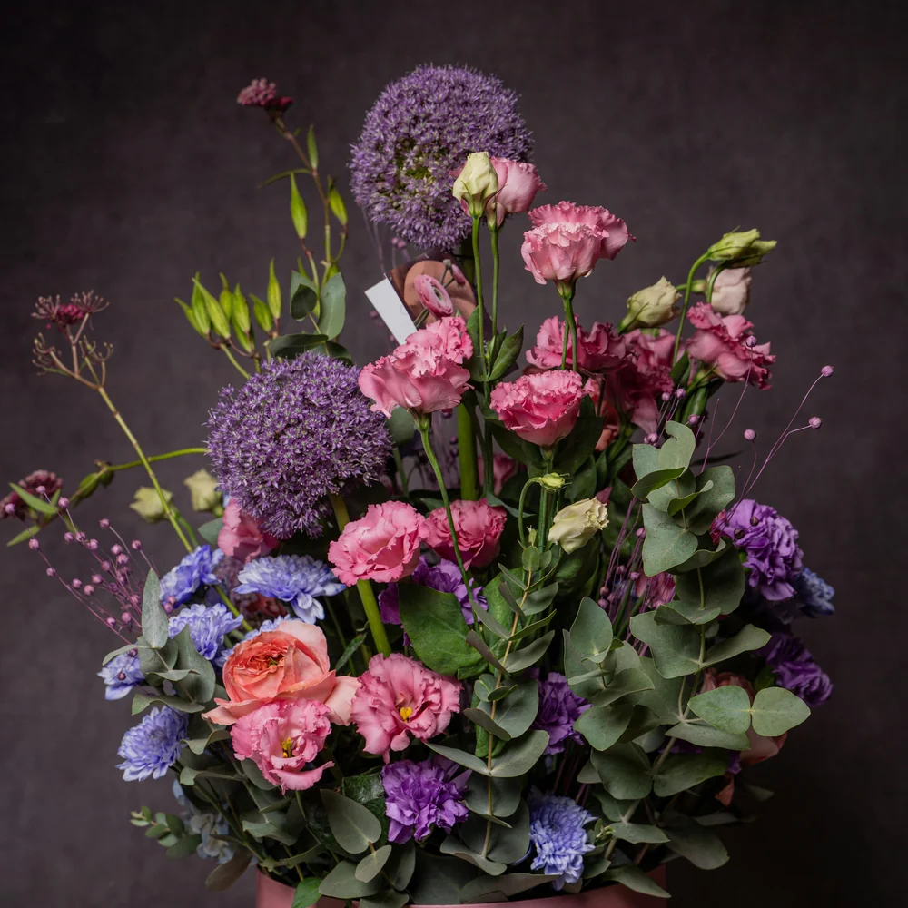 A pink and purple arrangement built into a tall hatbox vase