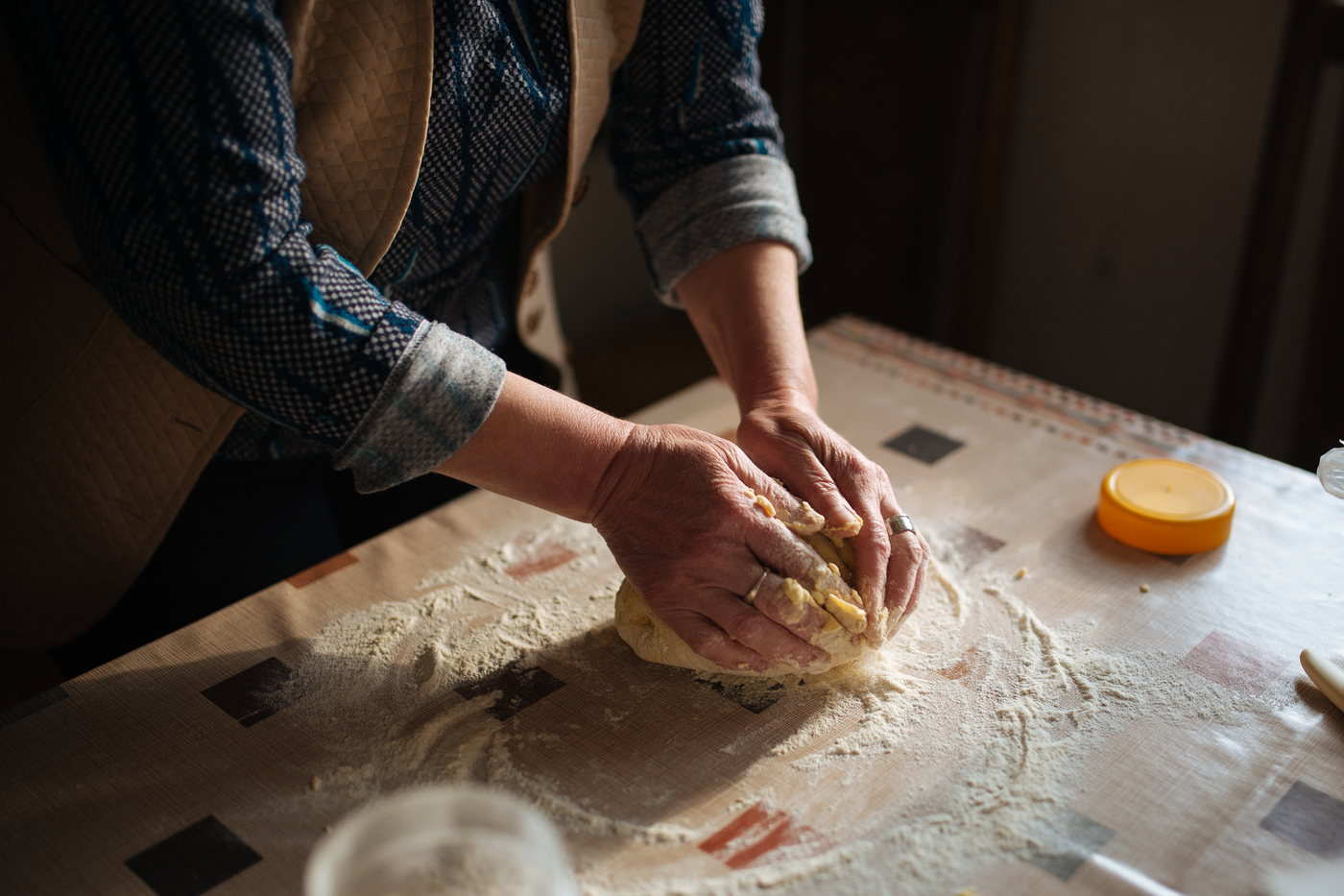 Floured hands kneading a pale round of bread dough on a work surface.