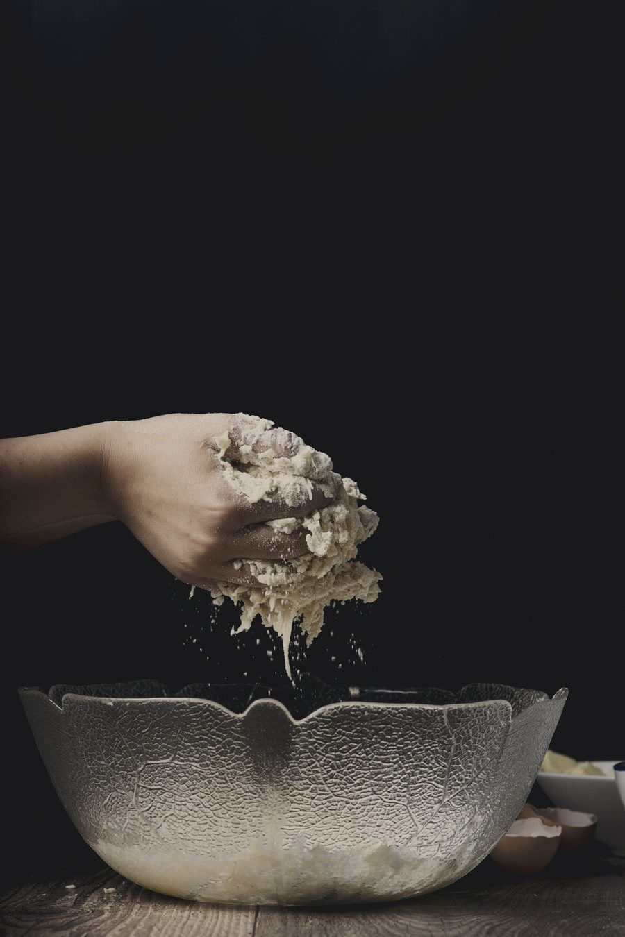 A hand releasing a loose handful of flour above a hammered metal bowl in a dark frame.