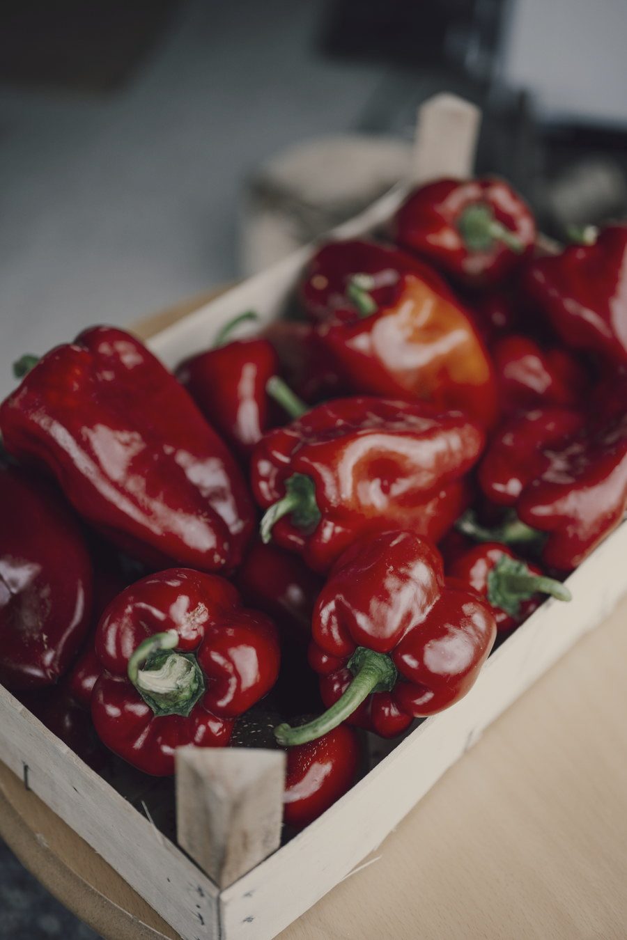 Red peppers with their stalks packed into a shallow pale wooden crate.
