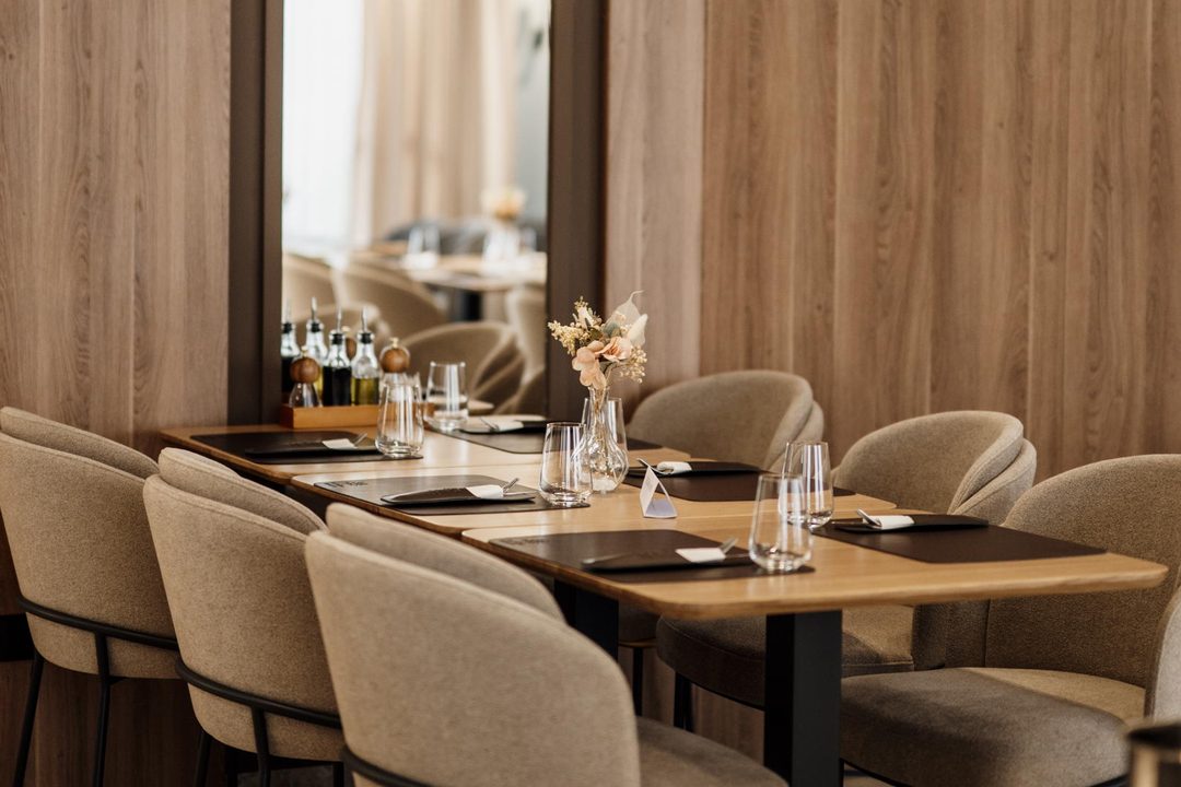 A long table set with placemats, glasses and a small dried arrangement in a room with wooden walls.