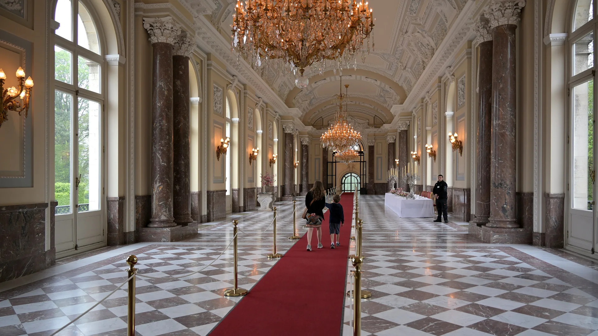 A grand hall lined with chandeliers above a carpeted aisle.