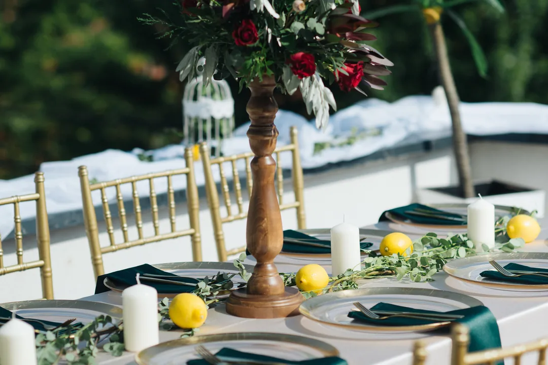 A long banquet table with gold chairs, green napkins and a tall floral centrepiece.