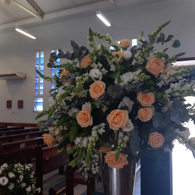 A tall ceremony arrangement of peach roses and eucalyptus beside a window.