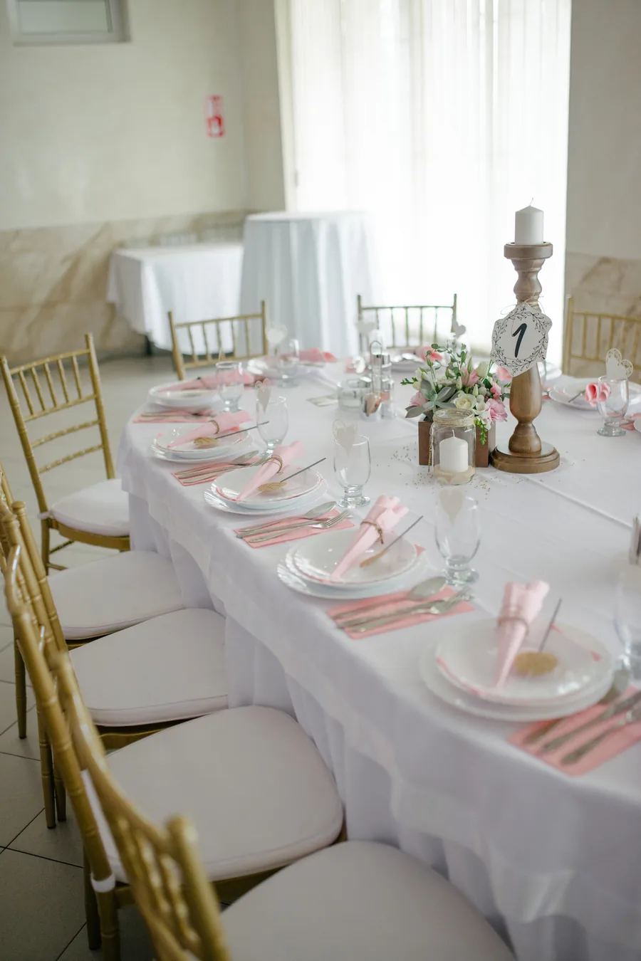 A long reception table set with white linen, gold chairs and ribboned place settings.