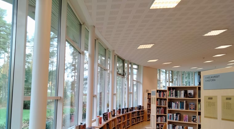A bright library reading room with low shelves running along a window wall